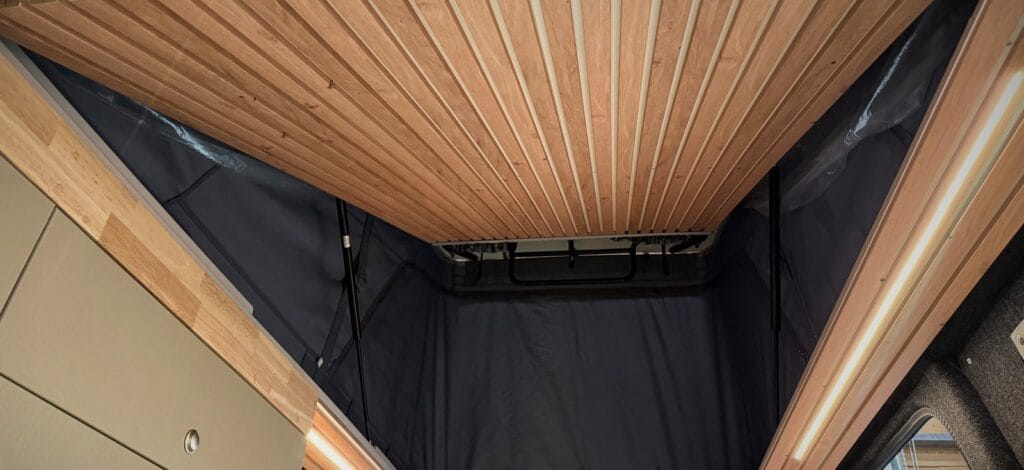 Van aménagé toit relevable par Karr Koncept : pavillon latté en bois sous le toit relevable ouvert, entre les montants en hévéa