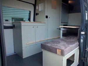 Fourgon atelier camping par Karr Koncept : le meuble cuisine et la banquette-coffre grise, porte latérale ouverte