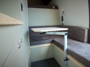 Fourgon atelier camping par Karr Koncept : la banquette en L grise et la table sur pied entourées de rangements