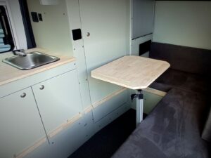Fourgon atelier camping par Karr Koncept : l'évier et la dînette avec table en hévéa massif sur pied réglable