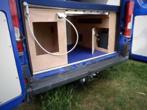 Grand van type camping-car par Karr Koncept : la soute arrière ouverte par les portes battantes, avec rangements techniques en bois