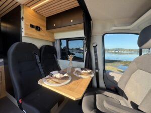 Tiny house roulante par Karr Koncept : la banquette et la table en chêne massif face au siège passager pivoté, vue sur l'eau