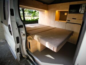 Van 4 couchages avec toit relevable par Karr Koncept : la banquette dépliée en lit, porte latérale ouverte sur le mobilier