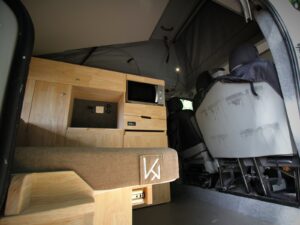 Van 4 couchages avec toit relevable par Karr Koncept : le meuble à micro-ondes en hévéa massif vu depuis la banquette