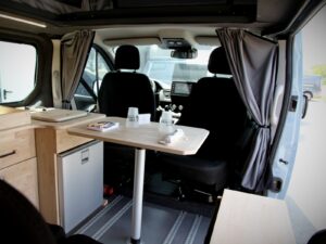 Van 4 places 4 couchages par Karr Koncept : la table dressée face aux sièges avant pivotés, entre les rideaux de cabine