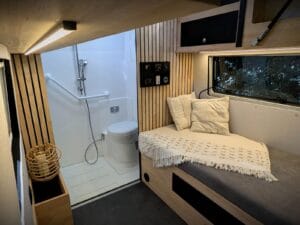 Van aménagé PMR par Karr Koncept : la banquette garnie de coussins près de la douche accessible, sous une réglette LED
