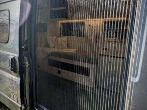 Van aménagé PMR par Karr Koncept : la moustiquaire plissée de la porte latérale devant la banquette éclairée en LED