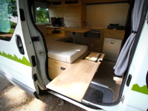 Van aménagé pour artisan par Karr Koncept : rallonge de lit en hévéa massif tirée vers la porte latérale ouverte