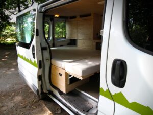 Van aménagé pour artisan par Karr Koncept : vue extérieure porte latérale ouverte sur le lit déplié et les meubles en hévéa