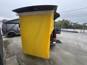 Van aménagé randonnée par Karr Koncept : rideau de douche jaune tendu sous le hayon ouvert, vue extérieure
