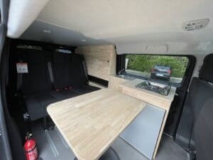 Van aménagé vanlife par Karr Koncept : le coin repas avec tablette en hévéa dépliée devant la banquette trois places