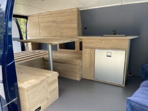 Van américain aménagé par Karr Koncept : banquette en L, table et bloc réfrigérateur en chêne massif vus de la porte latérale