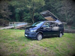 Van bohème par Karr Koncept : le Transporter noir garé dans une prairie, toit relevable ouvert
