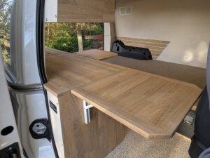 Van compact aménagé par Karr Koncept : la tablette en chêne massif dépliée côté porte latérale, face au couchage