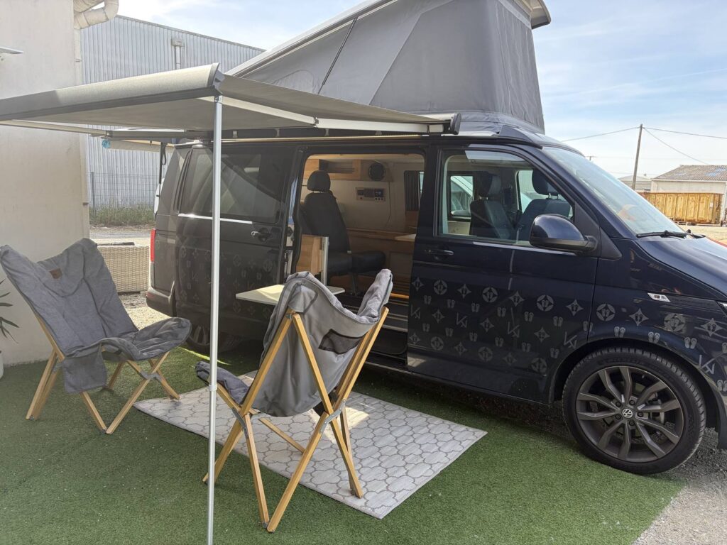 Le van de démonstration Karr Koncept 2025 au soleil, store déroulé et fauteuils devant la porte latérale ouverte