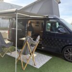 Le van de démonstration Karr Koncept 2025 au soleil, store déroulé et fauteuils devant la porte latérale ouverte