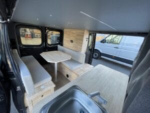 Van démontable amovible par Karr Koncept : salon avec deux banquettes et table vu depuis l'évier, porte latérale ouverte
