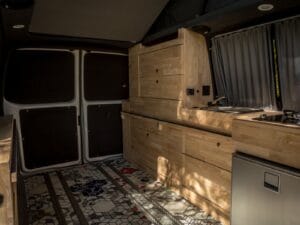 Van familial 5 places par Karr Koncept : l'espace arrière dégagé avec rails au sol, meuble cuisine en hévéa le long de la paroi