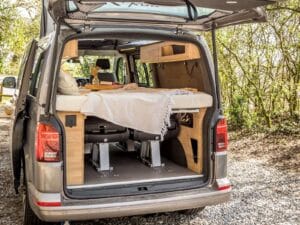 Van modulable par Karr Koncept : vue par le hayon ouvert sur le lit déplié au-dessus des sièges, cadre en chêne