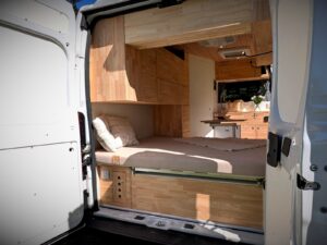 Vivre dans un van par Karr Koncept : les portes arrière ouvertes sur le lit fixe et les placards en hévéa massif